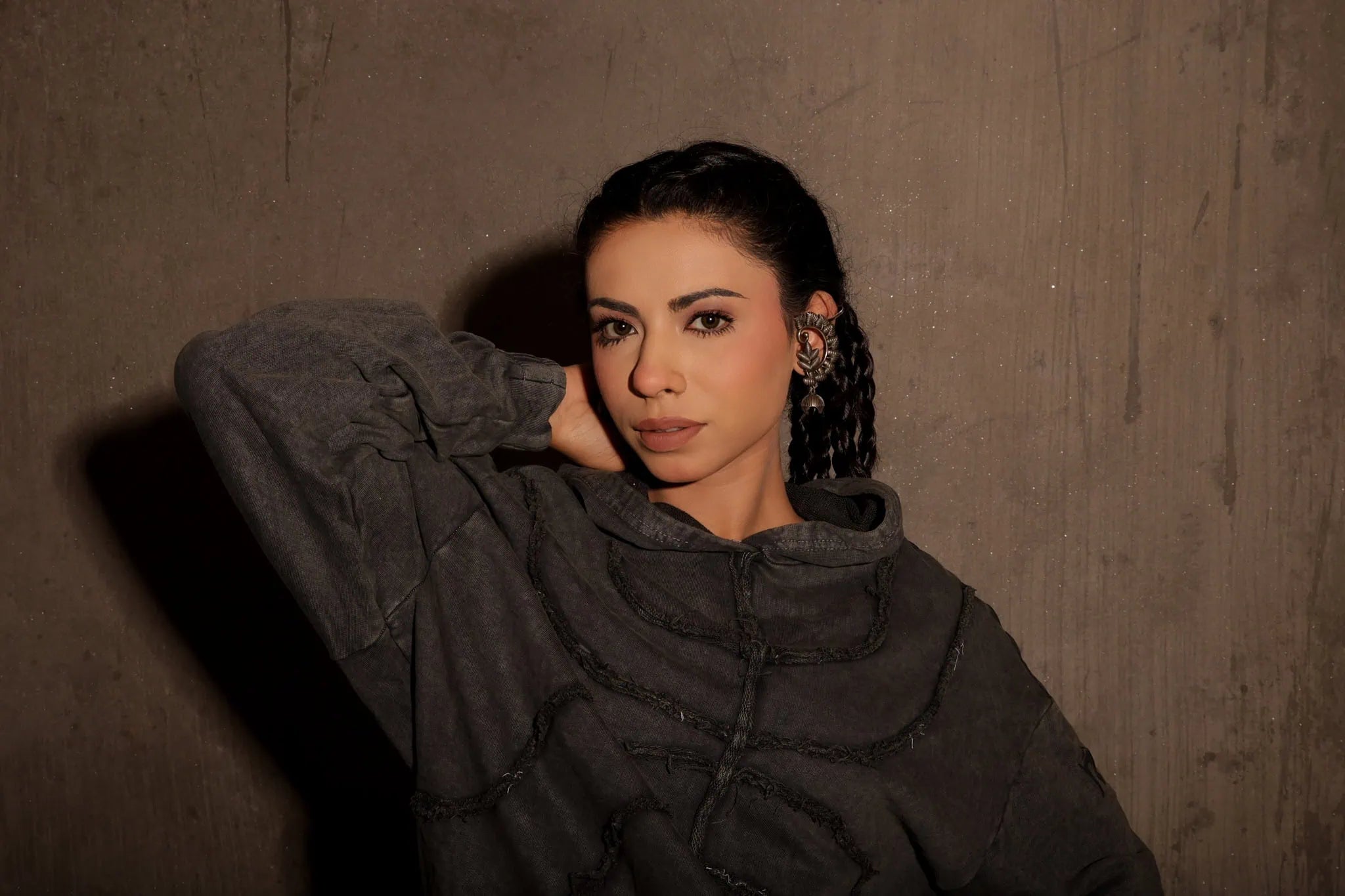 Woman wearing a dark gray hoodie against a textured brown wall