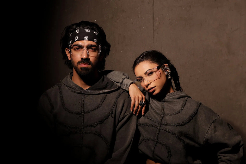 Two people wearing dark hoodies against a brown background