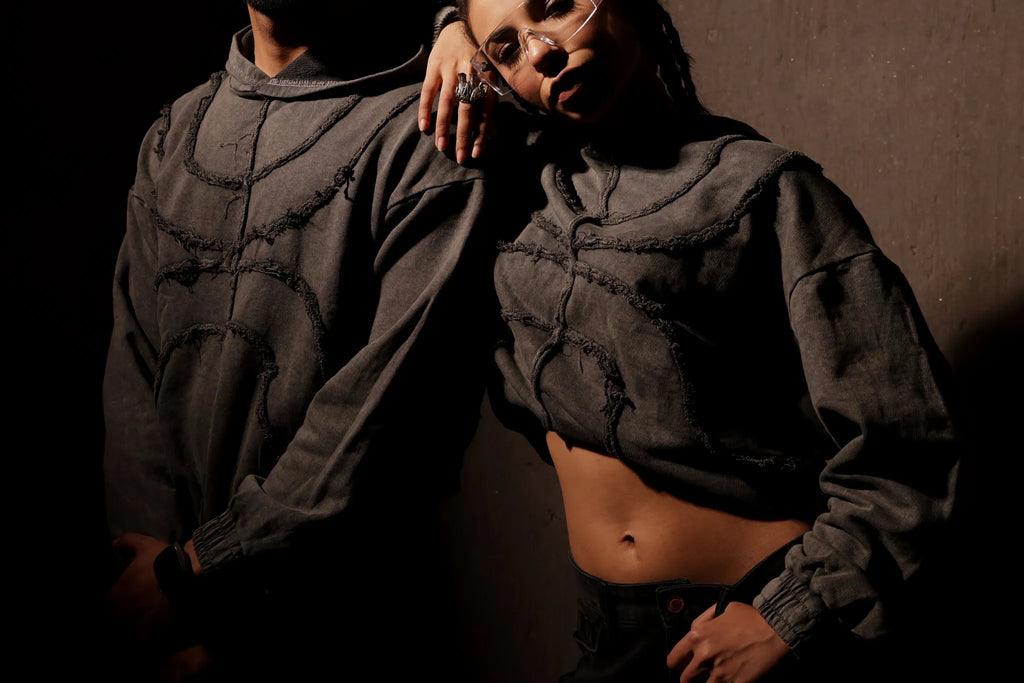 Two people wearing dark hoodies against a dark background