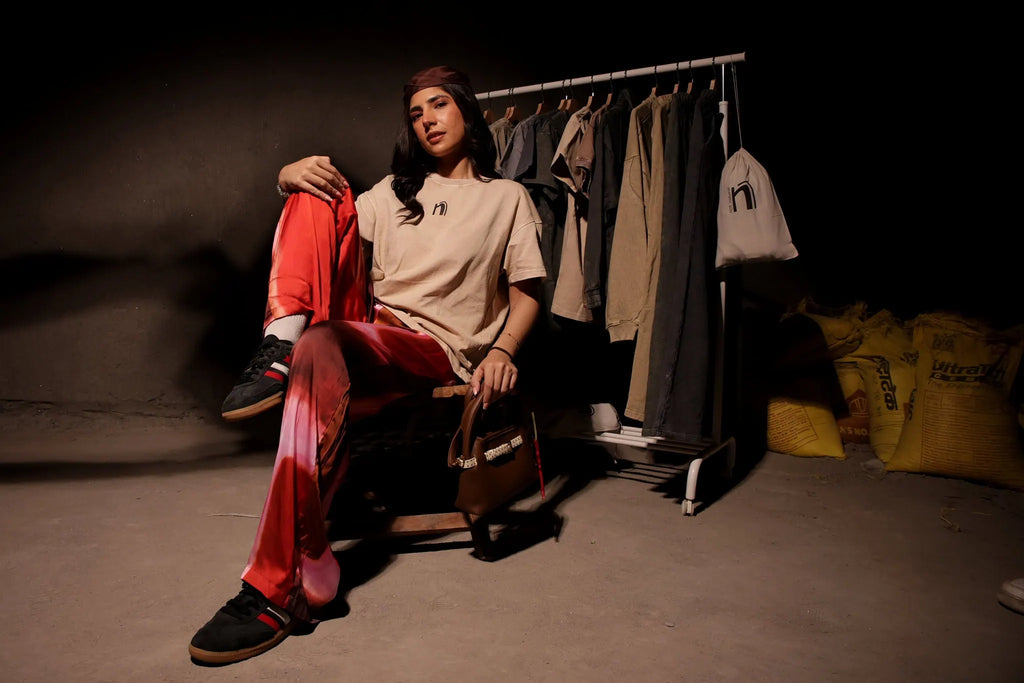 Person sitting on a stool in a room with clothing racks and bags.