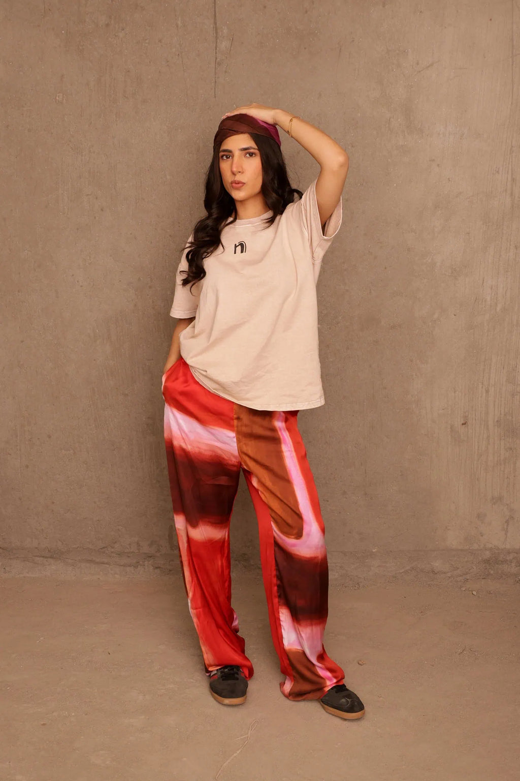 Woman wearing a beige top and red tie-dye pants against a plain wall.