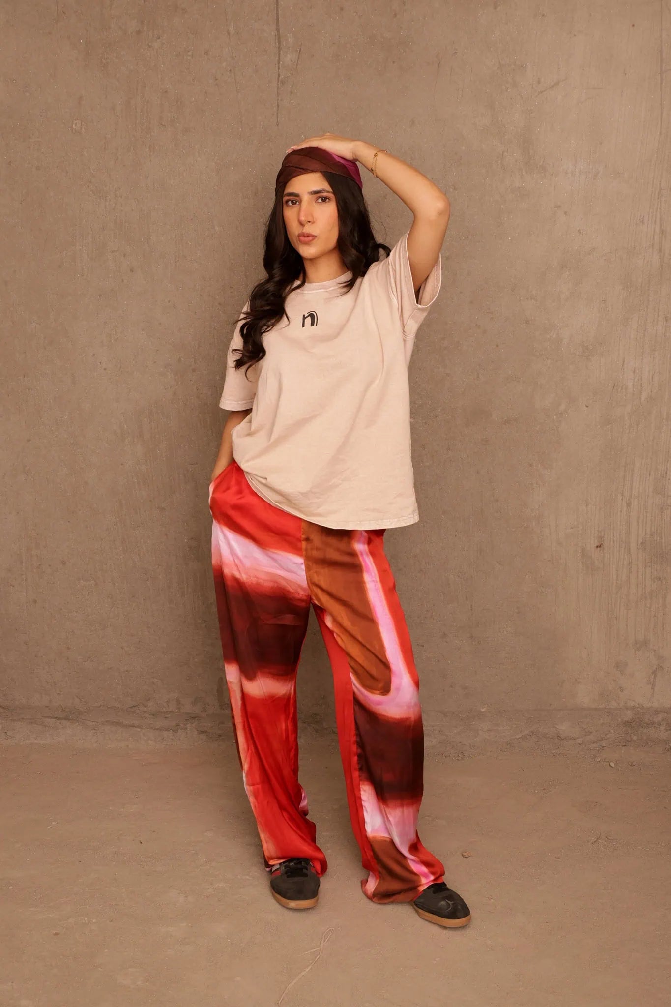Woman wearing a beige top and red tie-dye pants against a plain wall.
