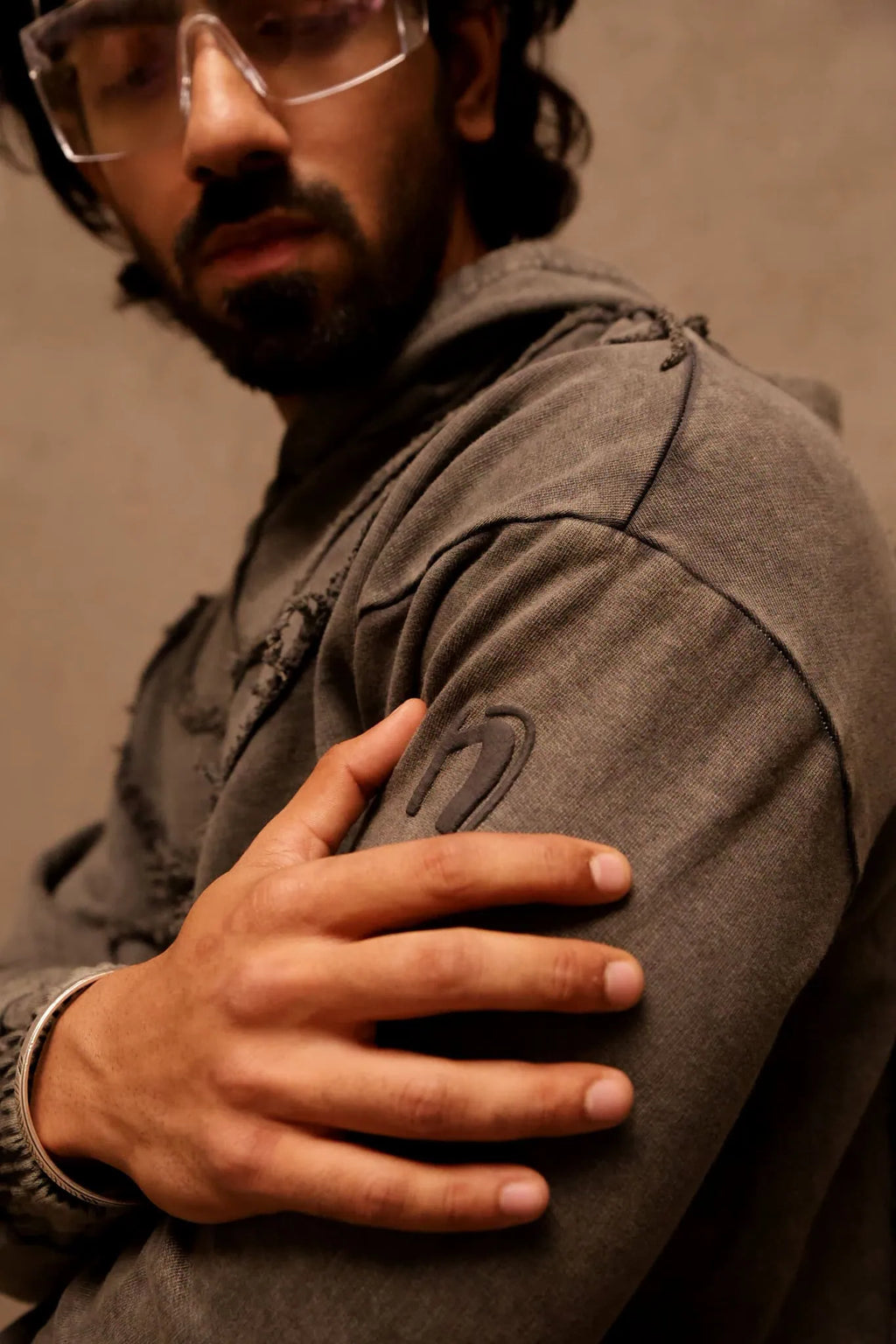 Man wearing a gray jacket with one arm crossed over his chest against a plain background