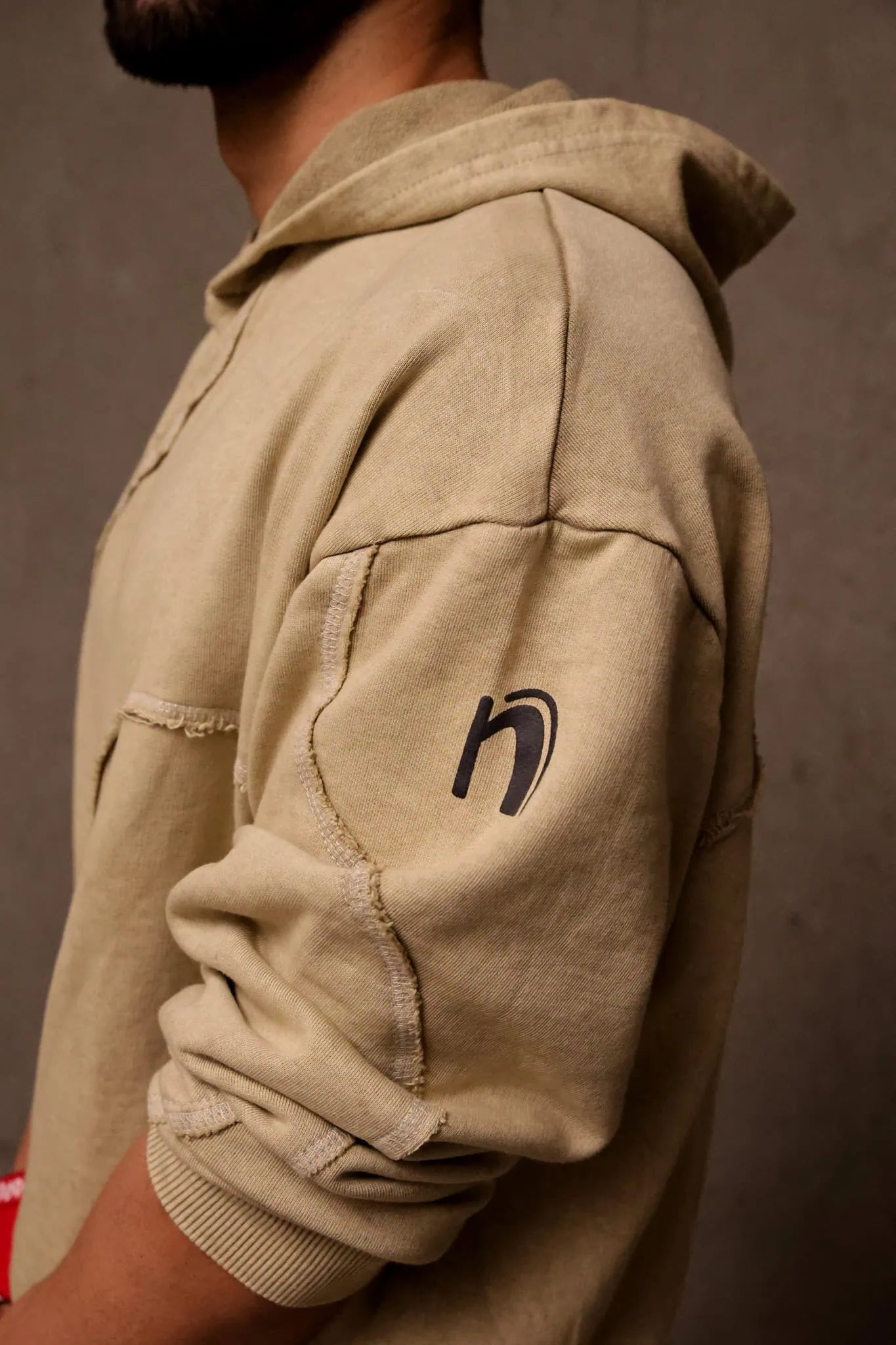 Beige hoodie with a logo on the sleeve against a brown background