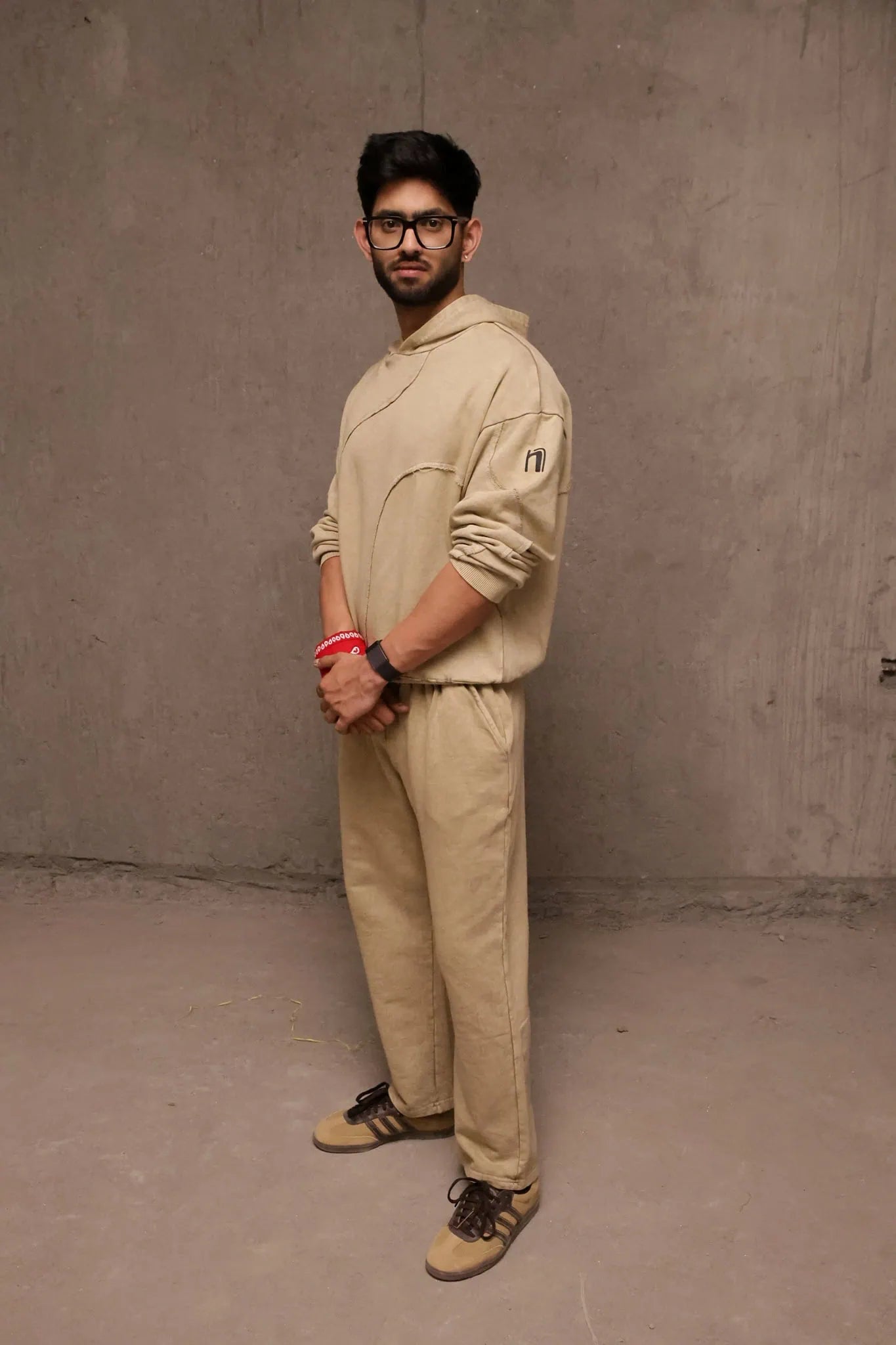 Man wearing a beige outfit standing against a plain wall.