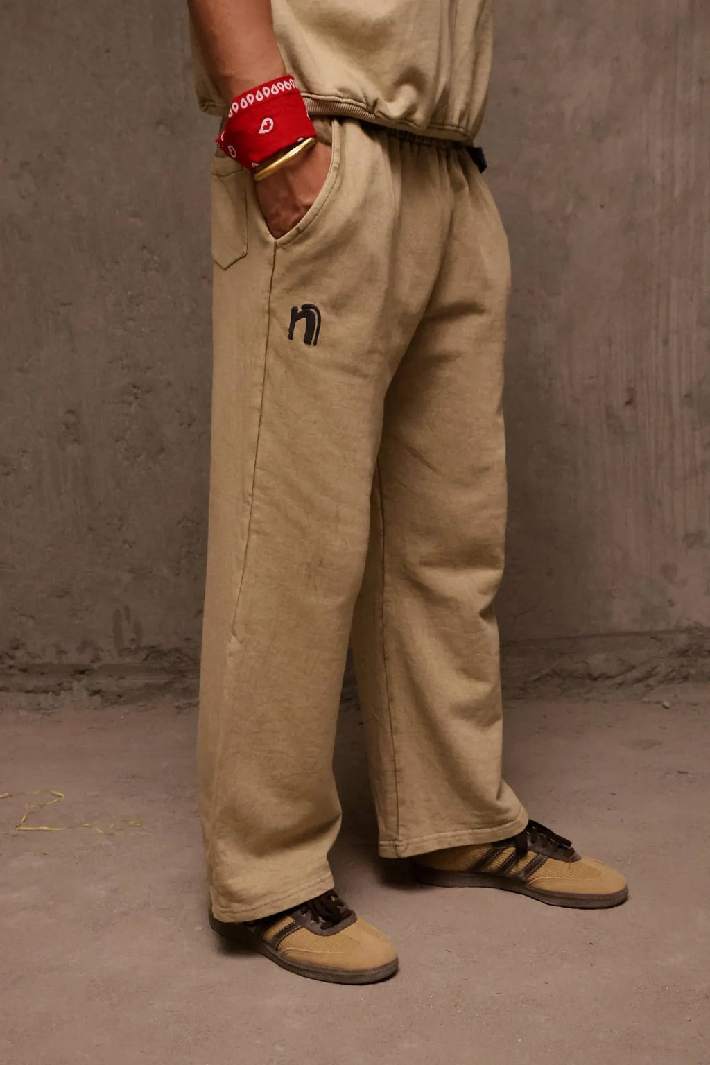 Person wearing beige pants with a small logo, standing against a plain background