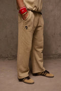 Person wearing beige pants with a small logo, standing against a plain background