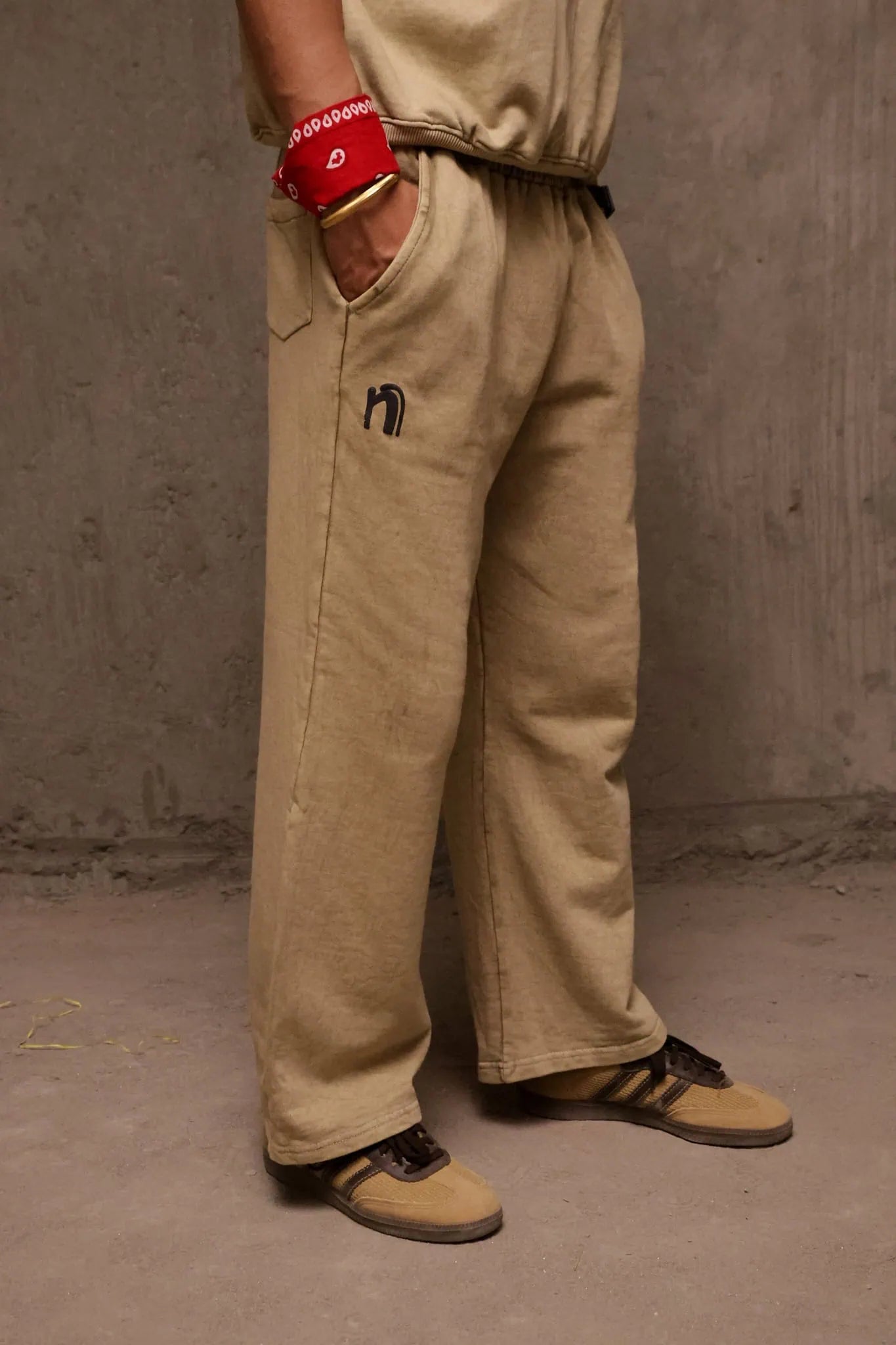 Person wearing beige pants with a small logo, standing against a plain background
