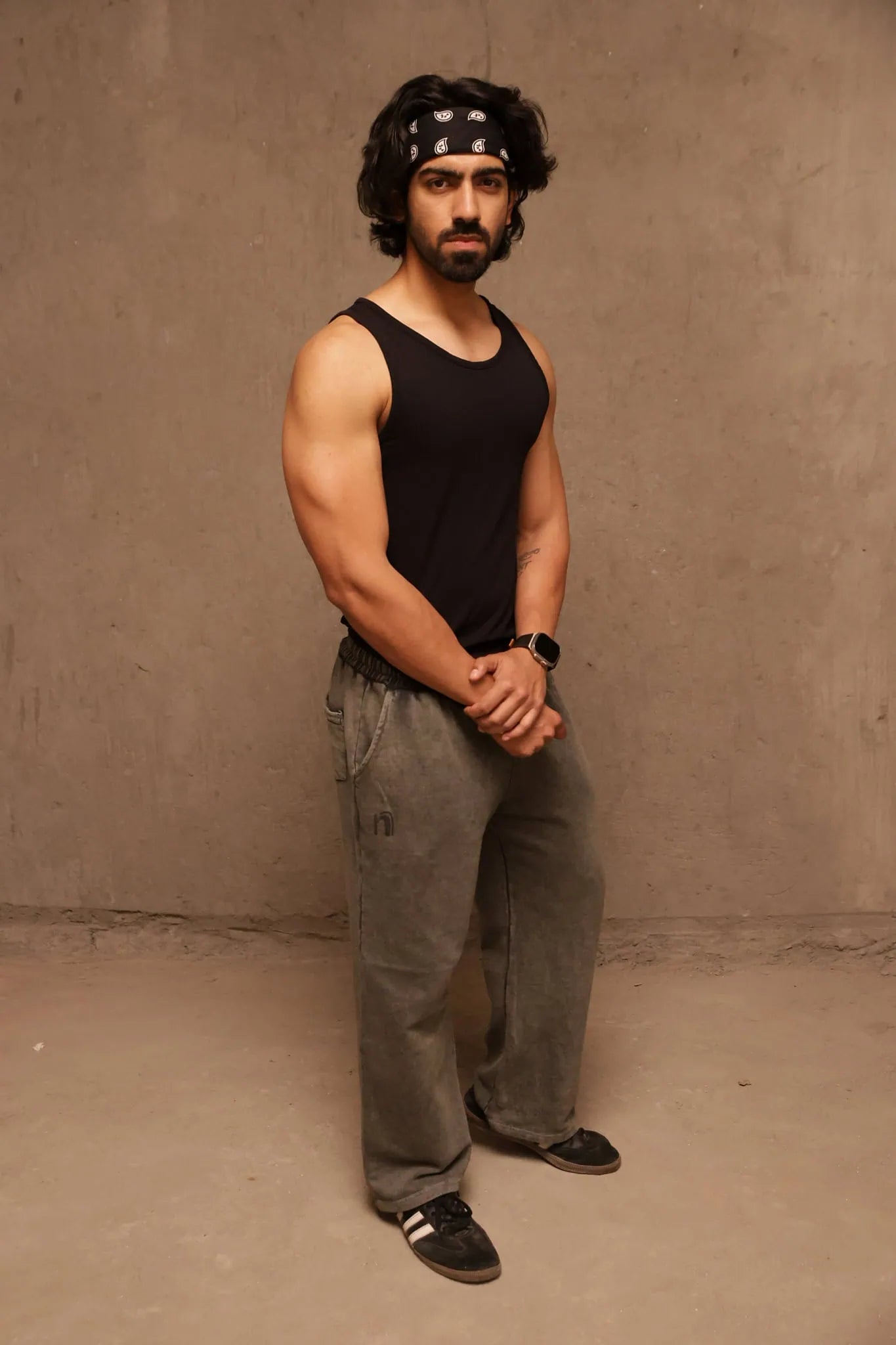 Man wearing a black tank top and gray pants against a beige wall.