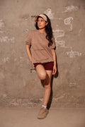 Woman wearing a brown t-shirt and red shorts against a textured wall.
