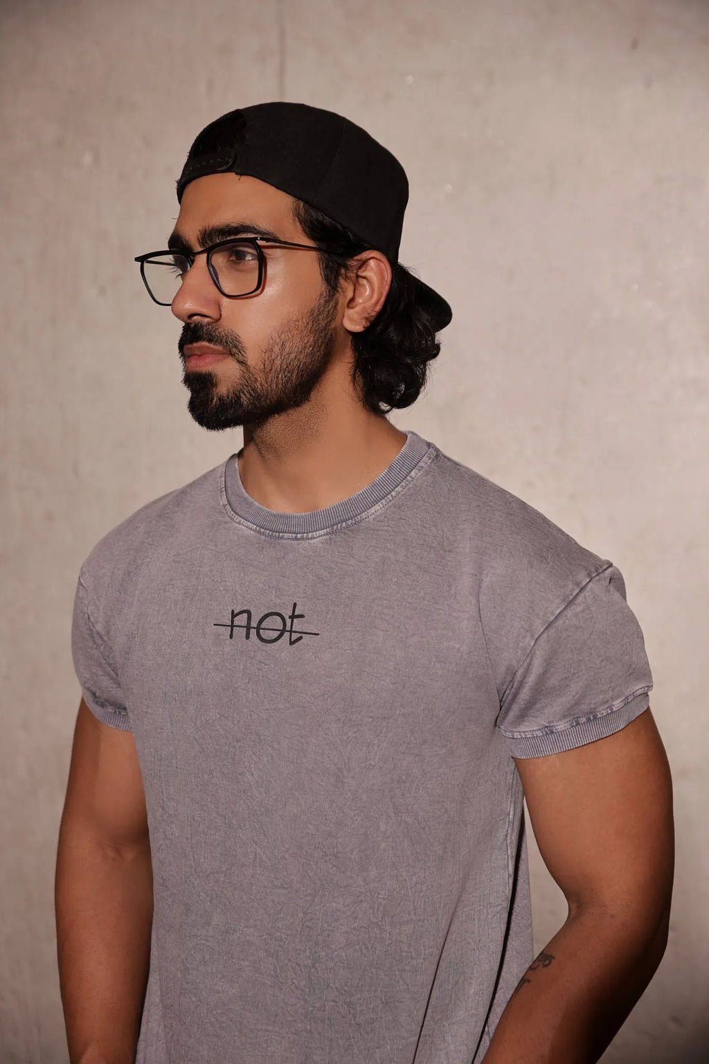 Man wearing a gray t-shirt with a logo and text, standing against a plain background