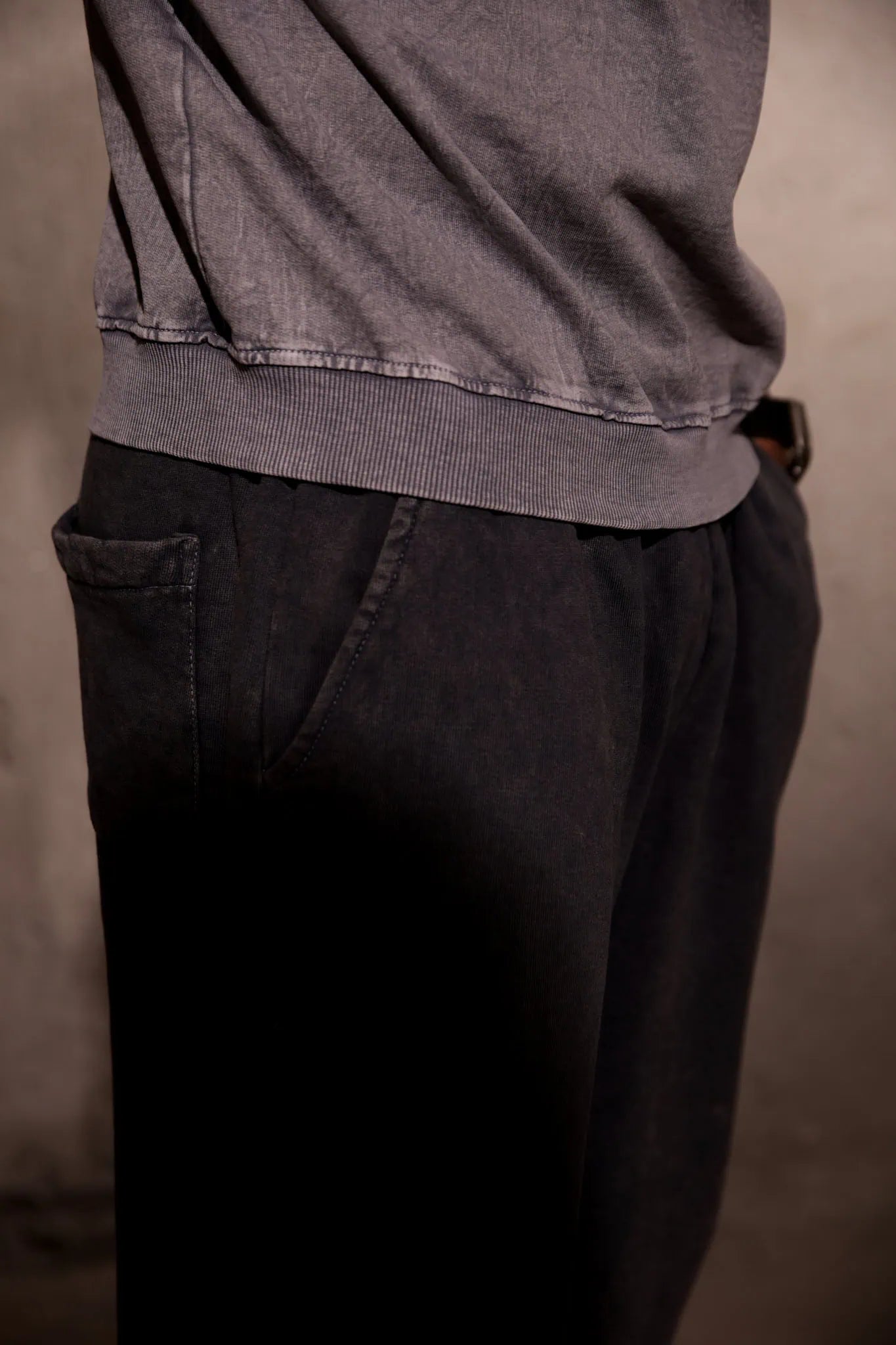 Person wearing a gray sweater and dark pants against a neutral background