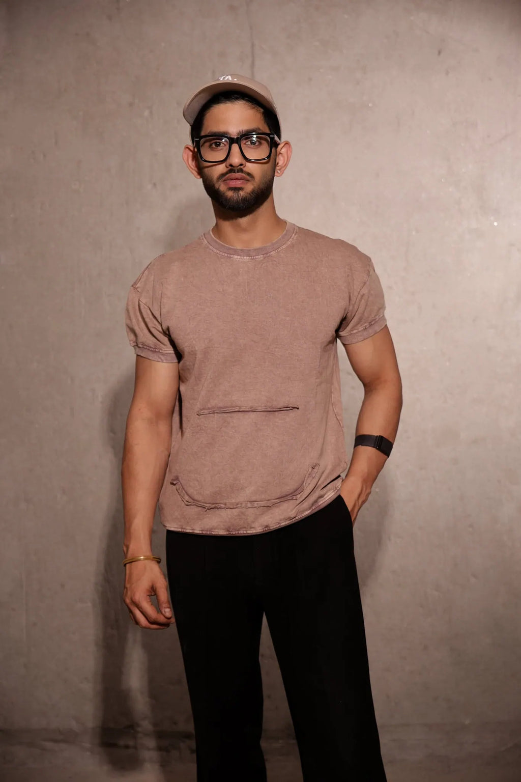 Man wearing a brown t-shirt and black pants against a plain background