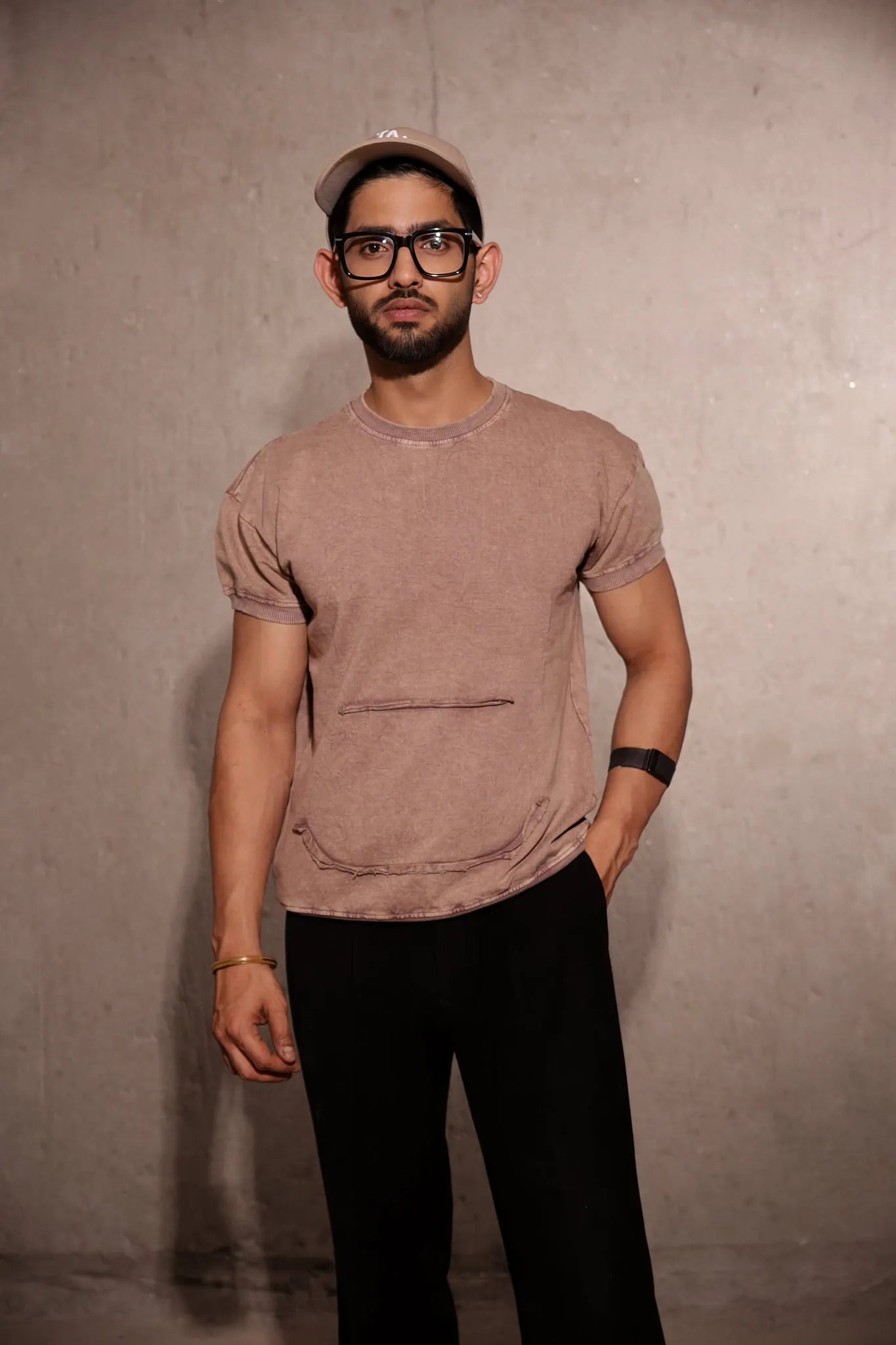 Man wearing a brown t-shirt and black pants against a plain background