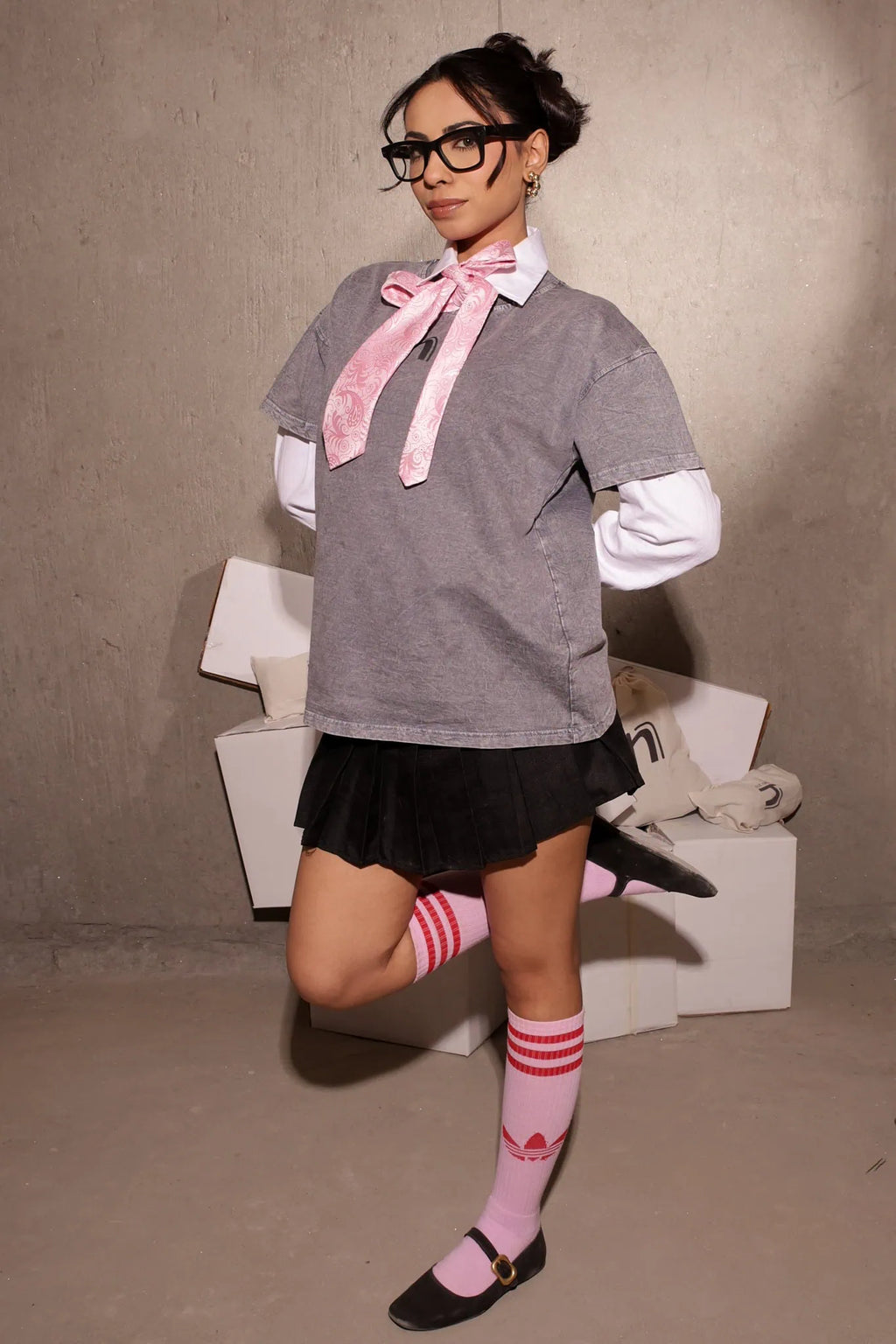 Person wearing a gray sweater, black skirt, and pink socks with a bow tie against a plain background