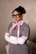 Person wearing a gray outfit with a pink bow tie against a plain background