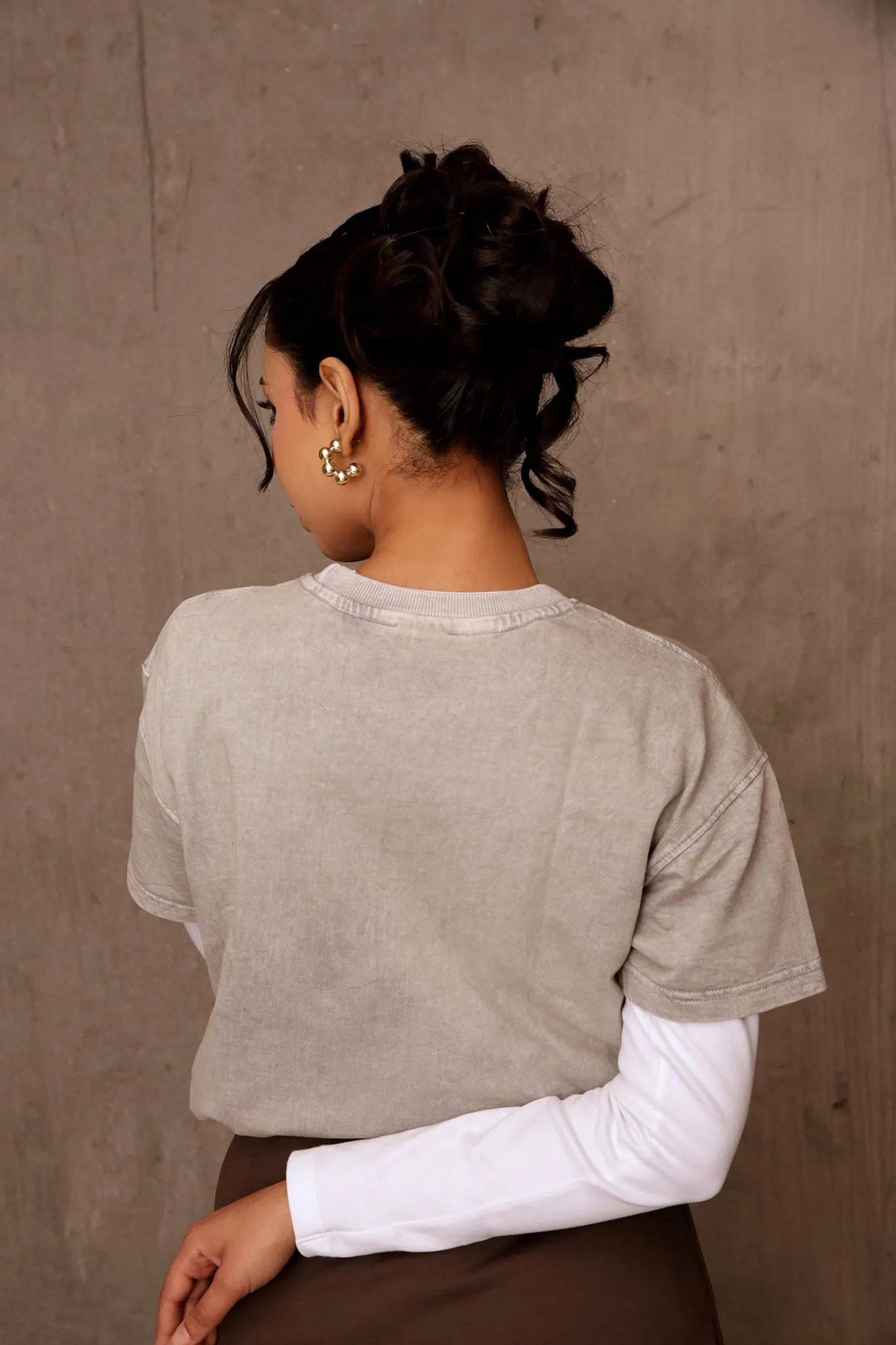Person wearing a light gray shirt with white sleeves against a beige wall