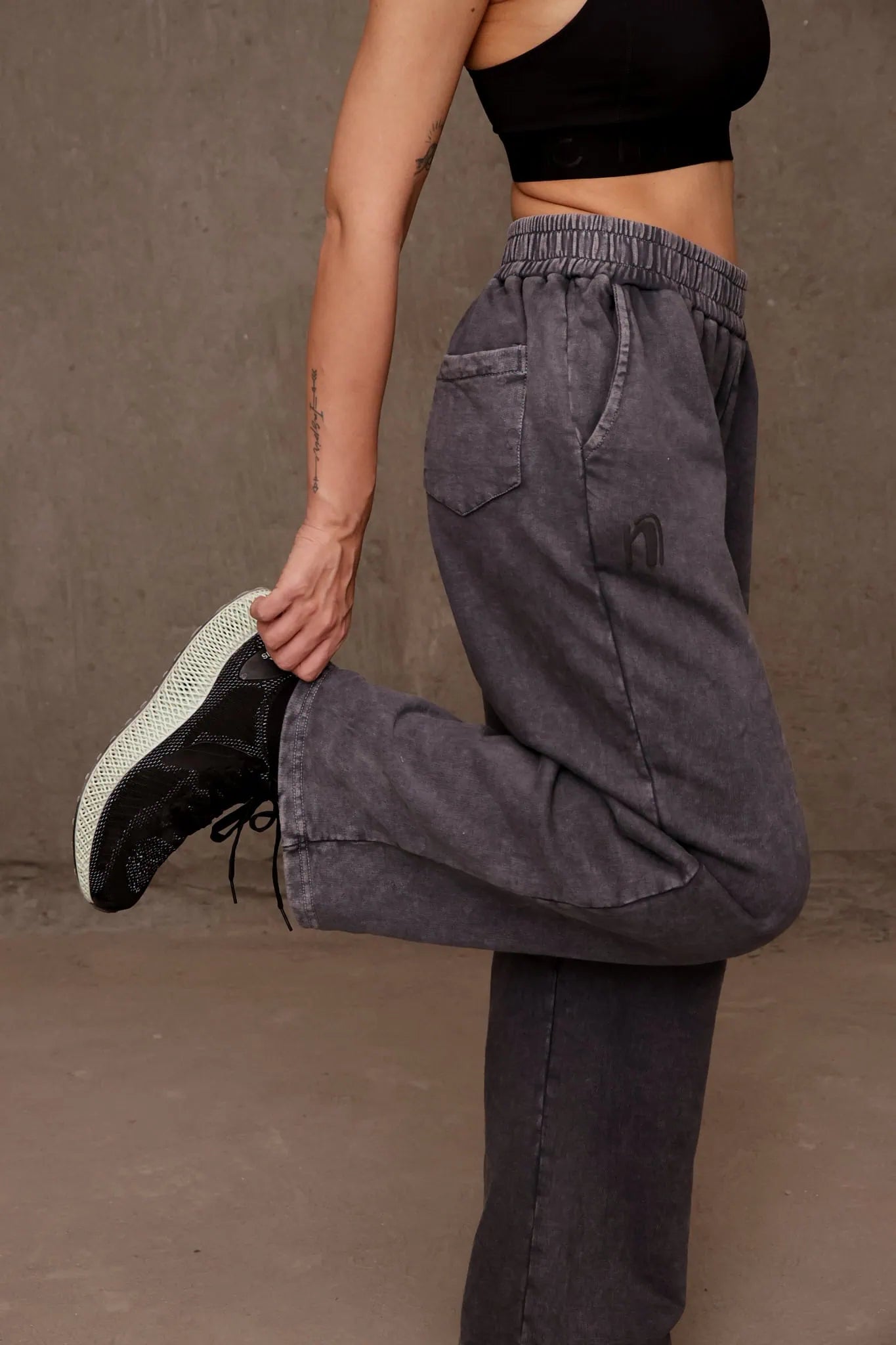 Person wearing dark gray pants and black shoes against a brown background