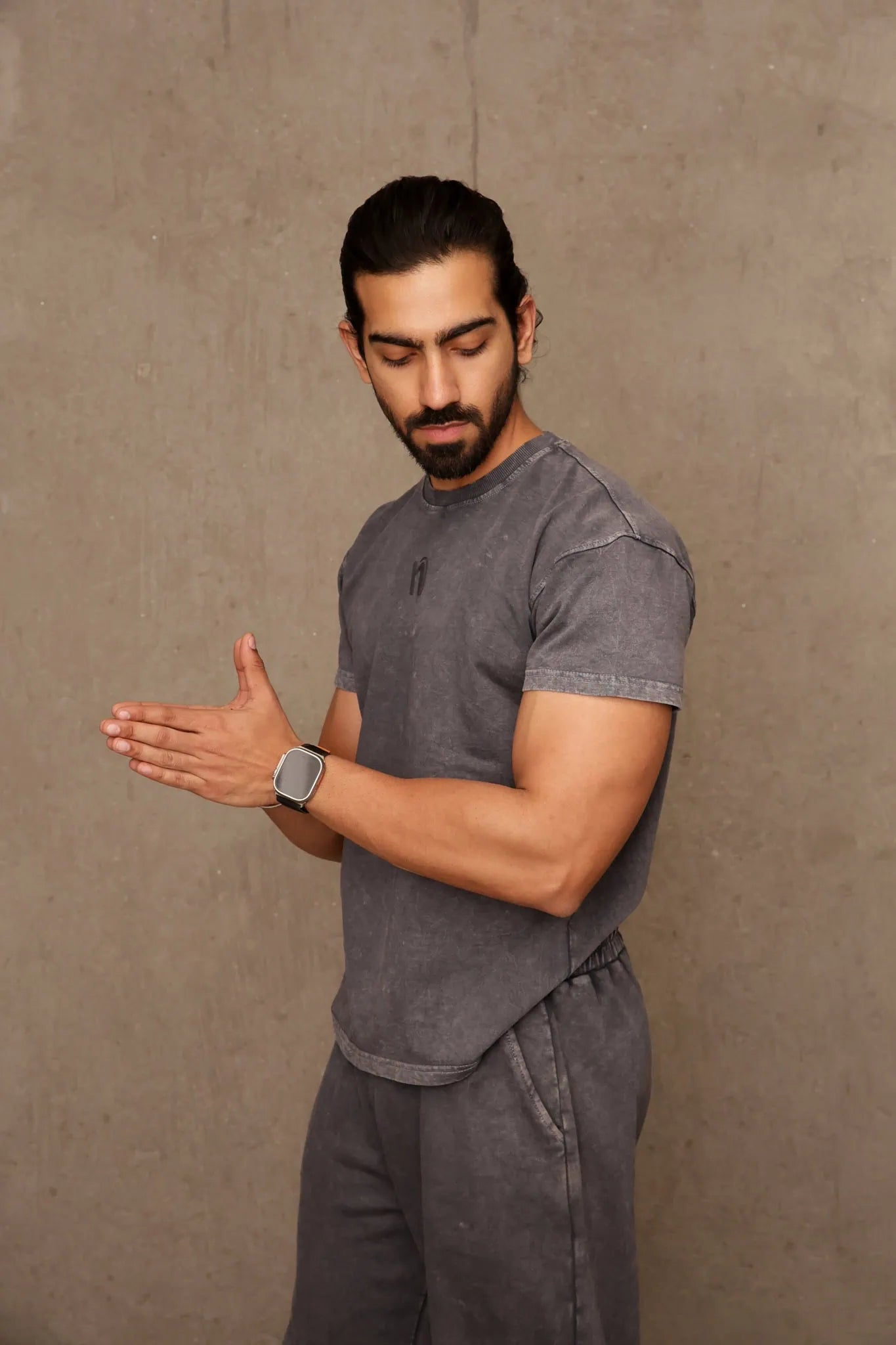 Man in gray t-shirt and pants standing against a beige wall