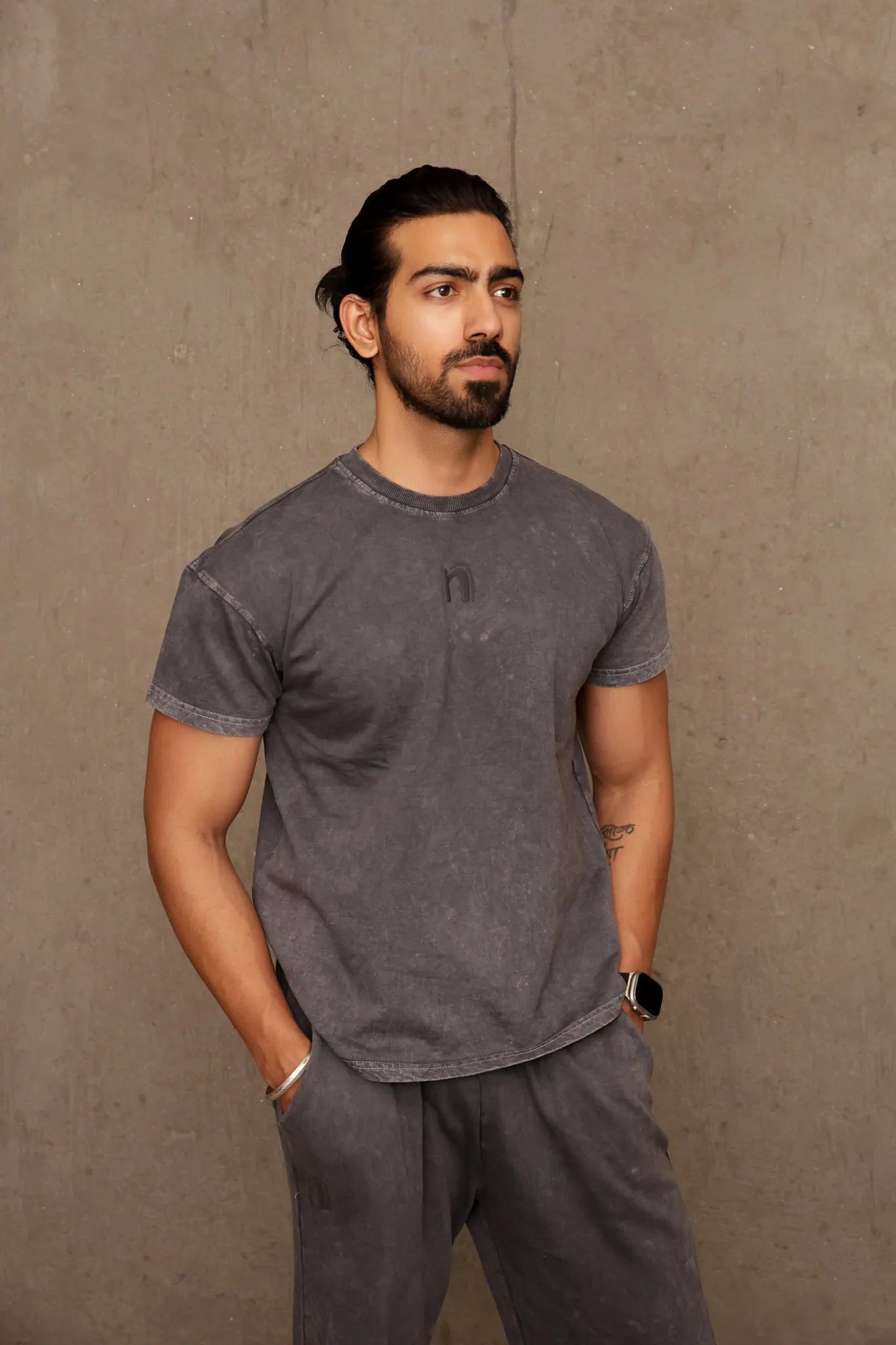 Man wearing a gray t-shirt and pants against a brown background