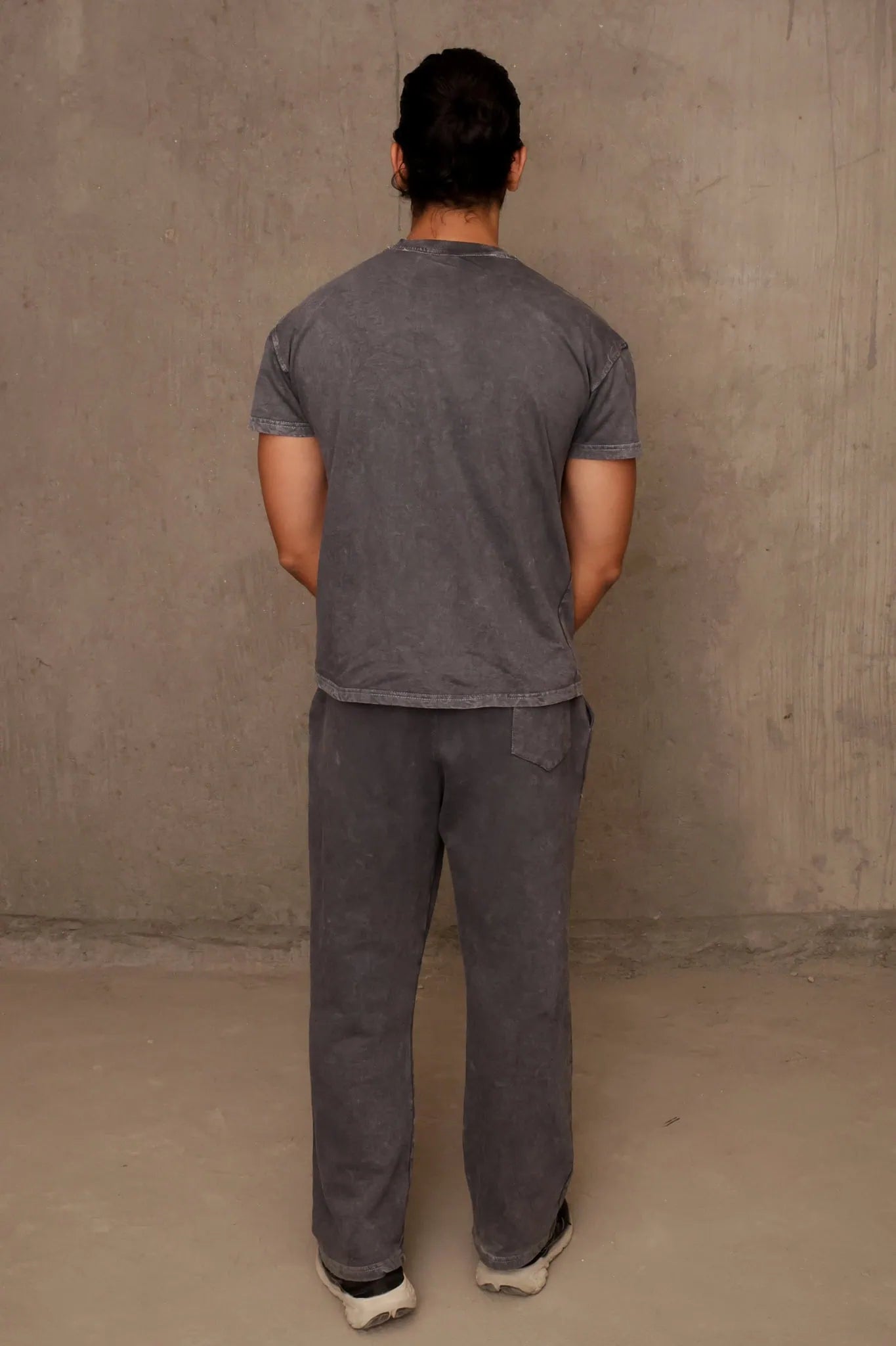 Person wearing a gray t-shirt and pants standing against a plain wall.