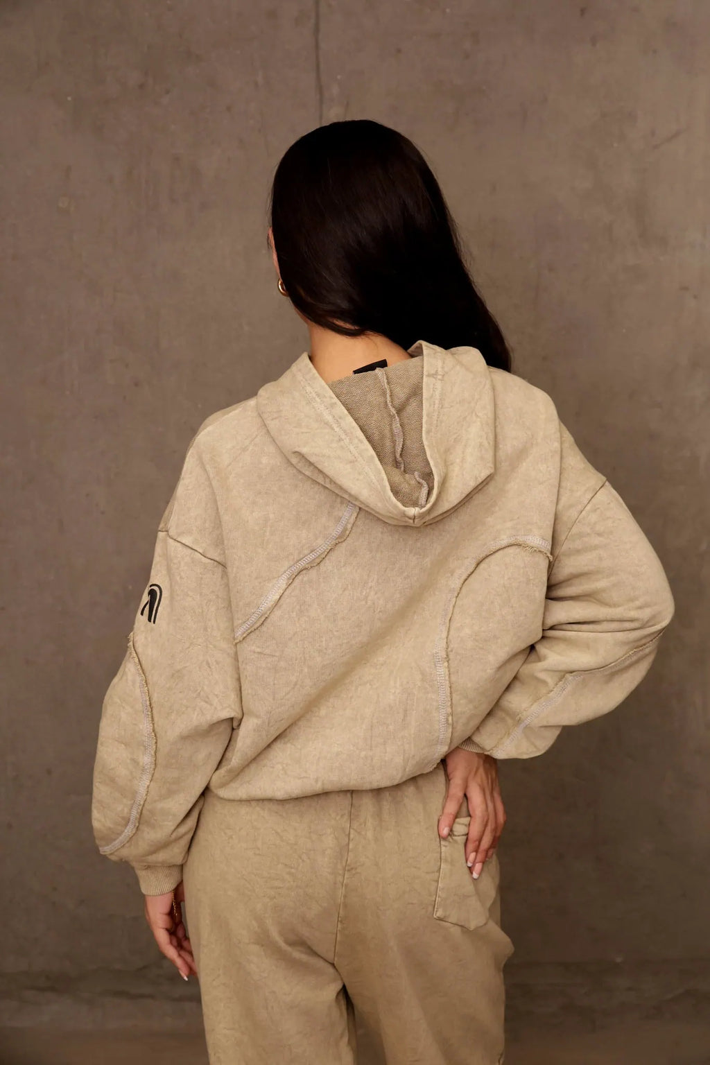 Person wearing a beige hoodie and pants against a brown background