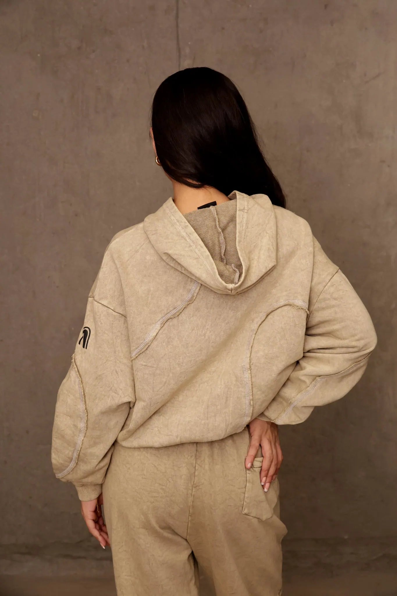 Person wearing a beige hoodie and pants against a brown background