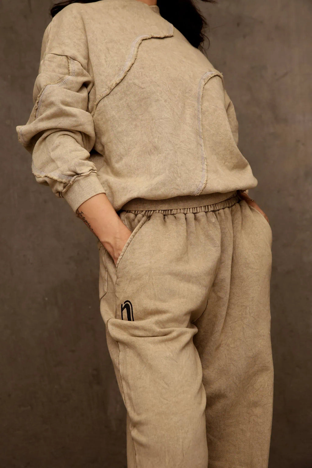 Person wearing a beige outfit against a brown background